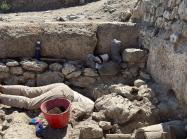 Excavation of certain physical features often requires archaeologists to get creative with digging methodologies. Wells, cisterns, and other subterranean features can be particularly challenging. Archeologist shown with head and torso in a hole as they work on site. 