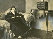 Wide World Photos, detail of Gertrude Stein sitting on a sofa in her Paris studio, with a portrait of her by Pablo Picasso, and other modern art paintings hanging on the wall behind her, May 1930. 