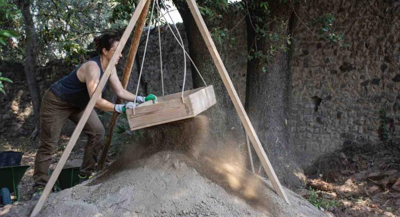 9758: Dana Zentgraf (excavator, PhD Student Christian-Albrechts-Universität Kiel) shakes soil through a sifter to look for finds that might otherwise be overlooked by the eye in the trench.