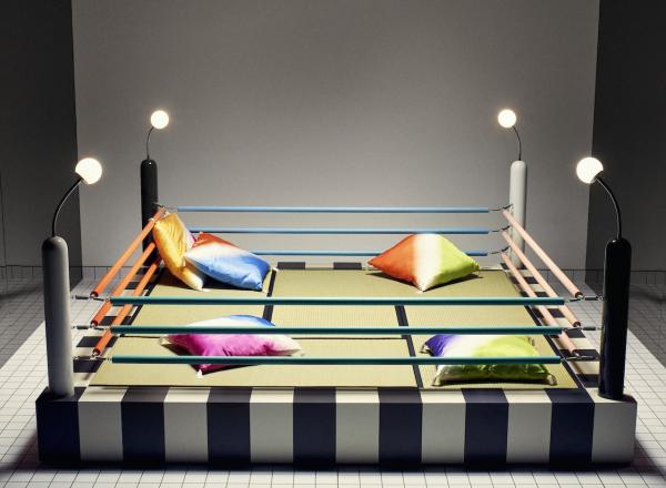 a bed or sitting area designed to resemble a boxing ring. With pillows in four corners and the ropes, lights and elevated platform of a ring.  